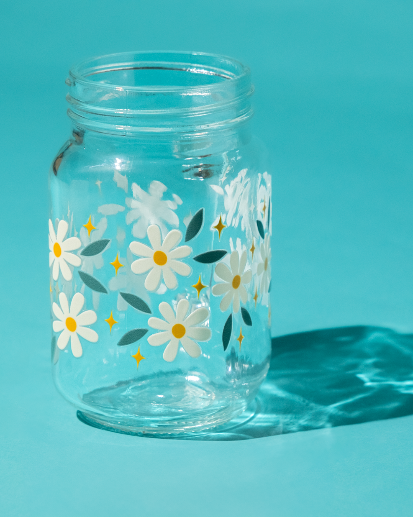 Clear glass jar with daisy pattern on a light blue background